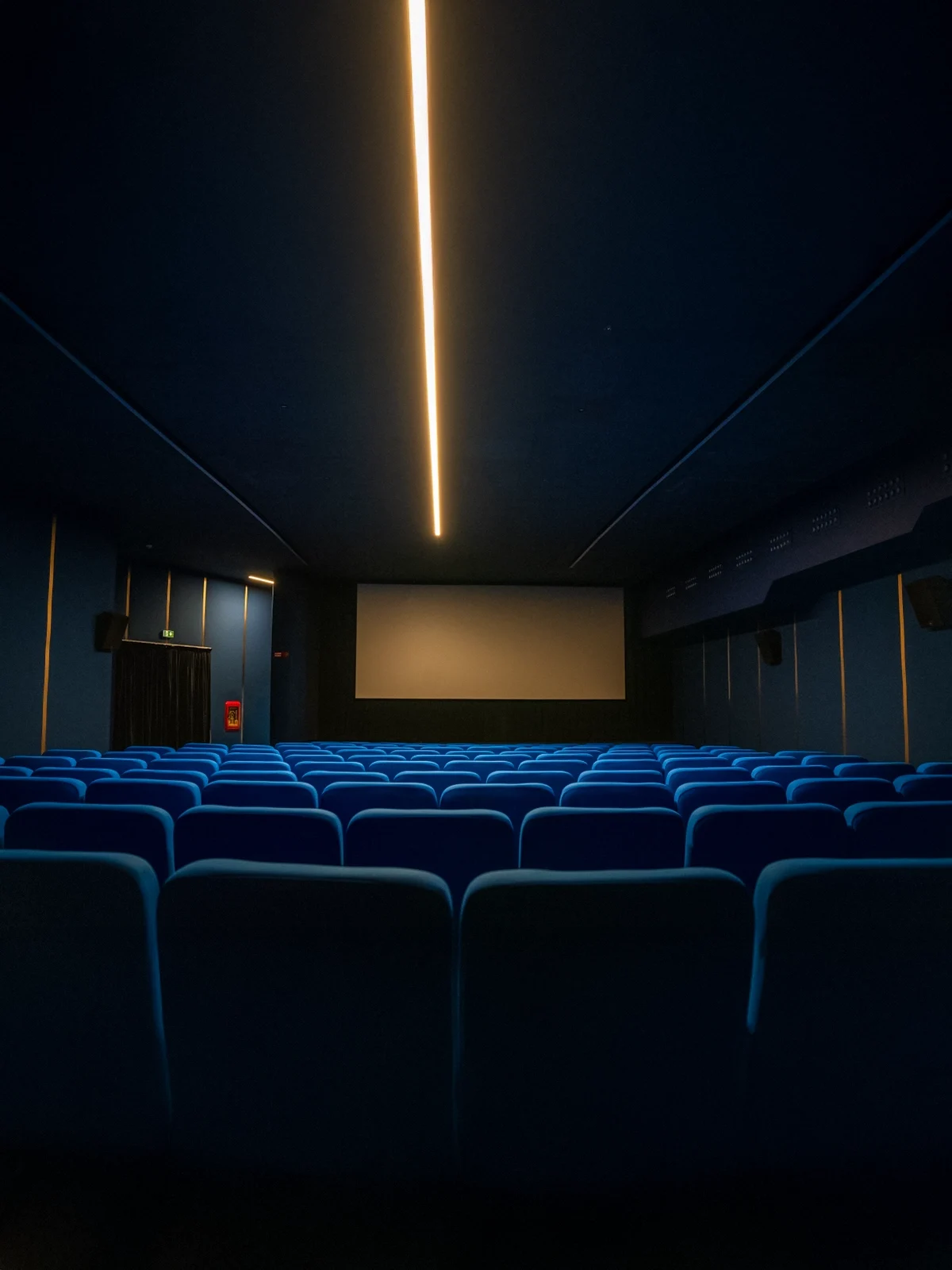 Sala interna del Cinema Eliseo a Torino dopo l&rsquo;intervento di riqualificazione architettonica, vista dal retro della sala con sedute blu e illuminazione lineare a soffitto