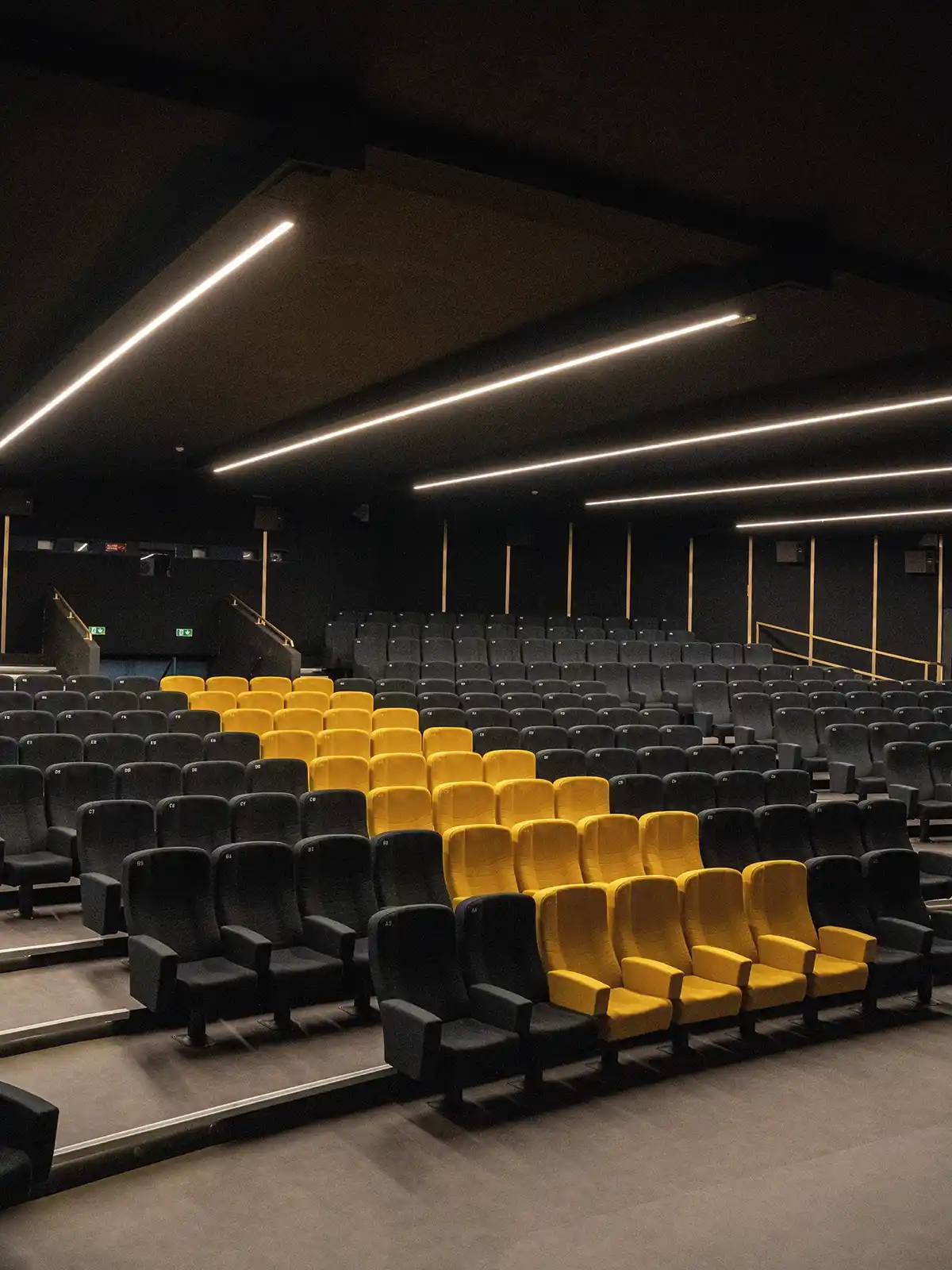 Sala interna del Cinema Eliseo a Torino dopo l&rsquo;intervento di riqualificazione architettonica, vista laterale con sedute nere e gialle e illuminazione lineare a soffitto