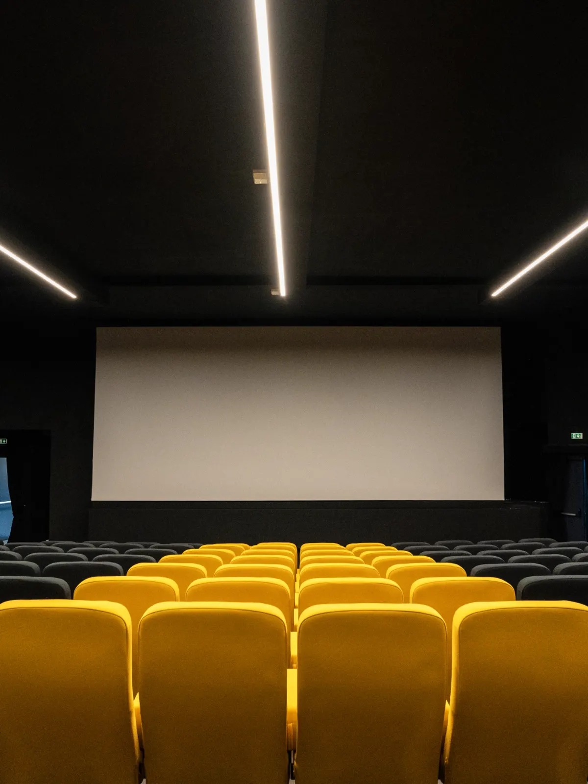 Sala interna del Cinema Eliseo a Torino dopo l&rsquo;intervento di riqualificazione architettonica, vista dal retro con sedute nere e gialle e illuminazione lineare a soffitto