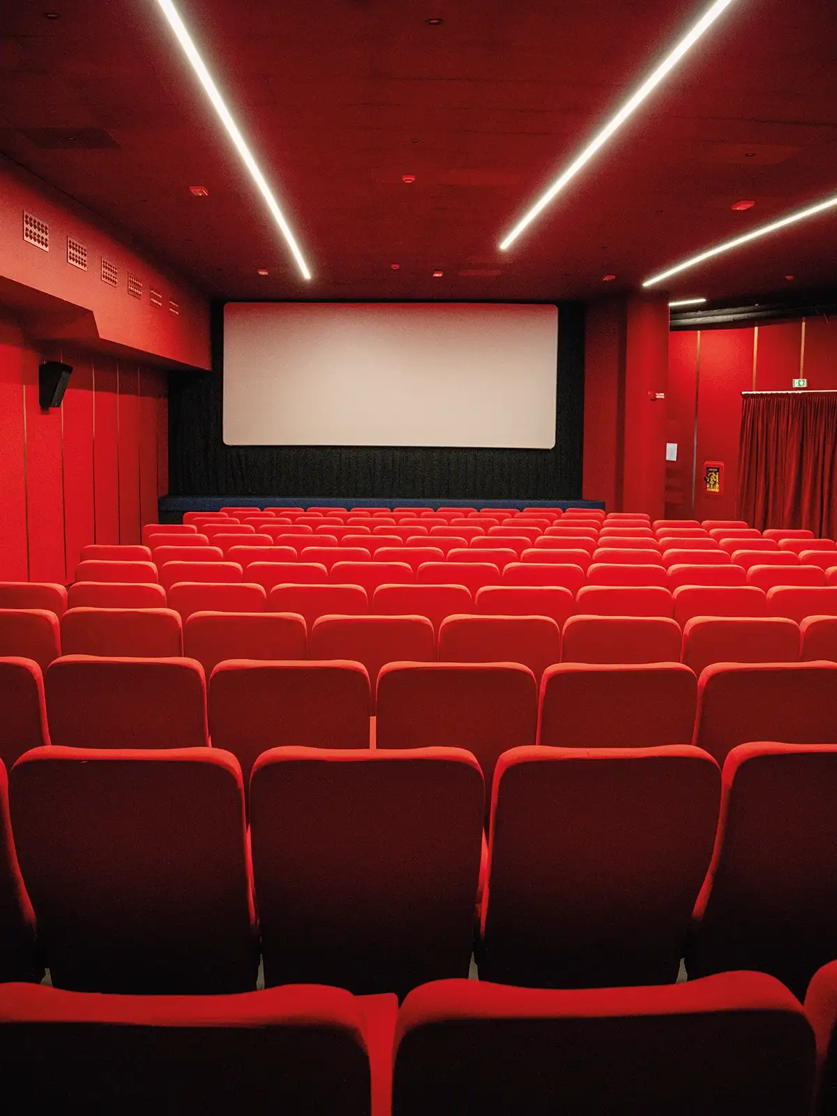 Sala interna del Cinema Eliseo a Torino dopo l&rsquo;intervento di riqualificazione architettonica, vista dal retro con sedute rosse e illuminazione lineare a soffitto
