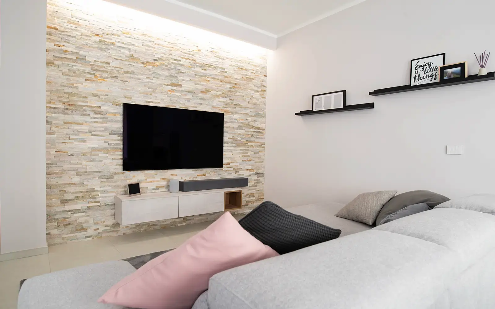 Zona living con parete TV rivestita in pietra materica e illuminazione integrata in appartamento contemporaneo a Torino
