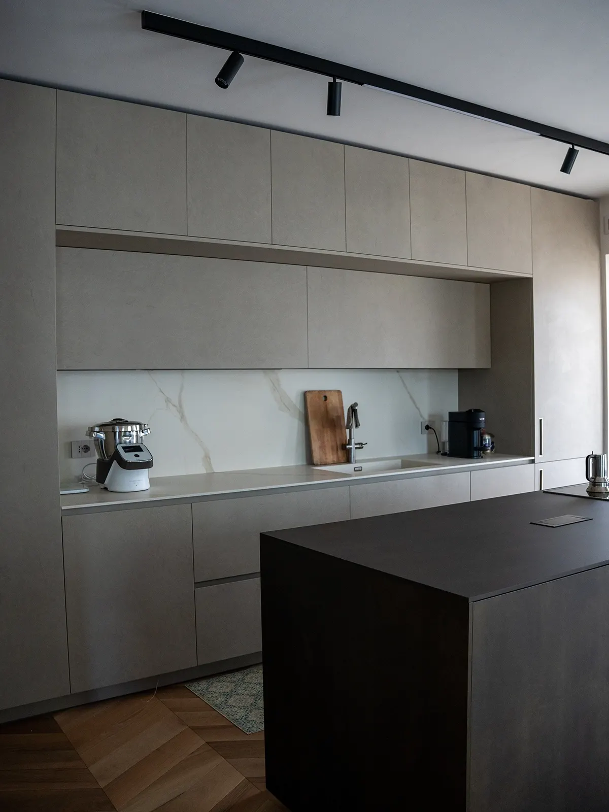 Cucina minimal su misura con isola centrale, finiture materiche e illuminazione a binario in un progetto di interior design a Torino