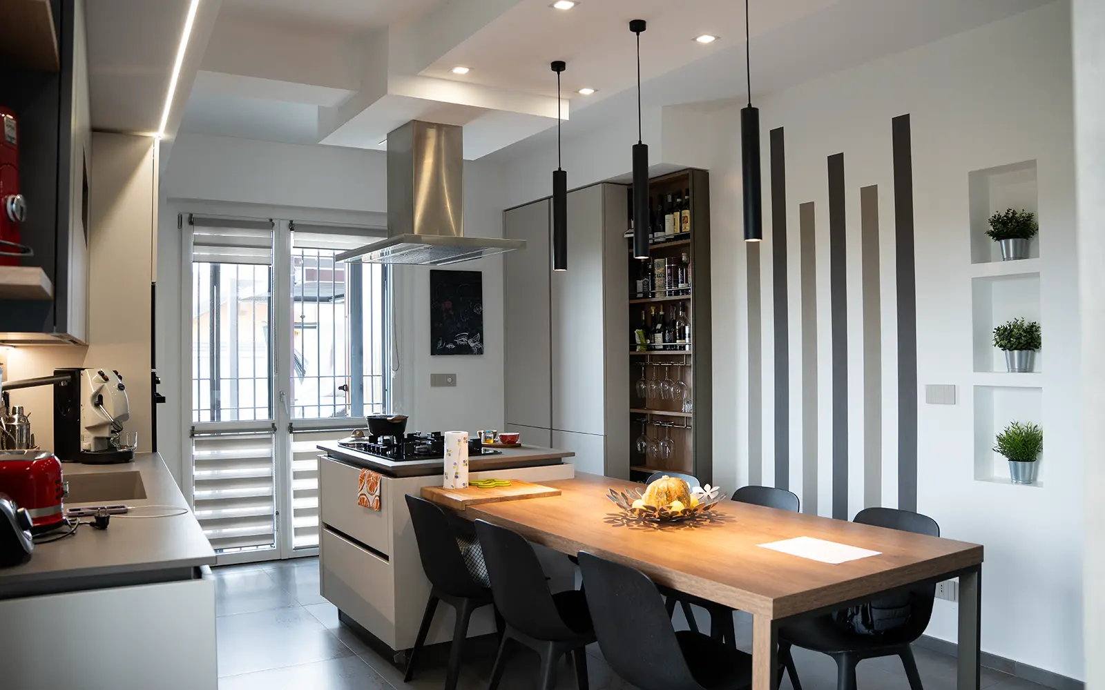 Interior design di cucina moderna con isola centrale, palette neutra e dettagli illuminotecnici in una villetta a schiera contemporanea a Torino.
