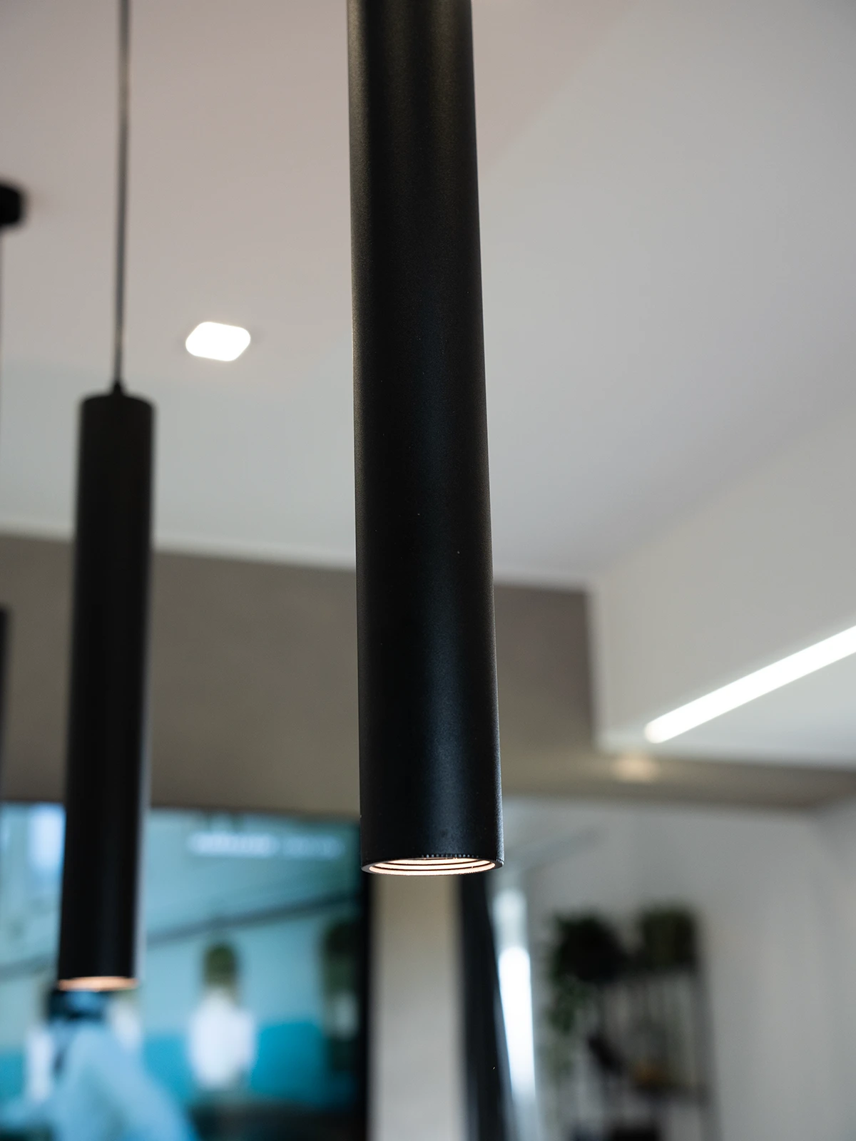 Dettaglio delle lampade a sospensione nere e dell&rsquo;illuminazione lineare integrate nella cucina di design di una villetta a Torino.