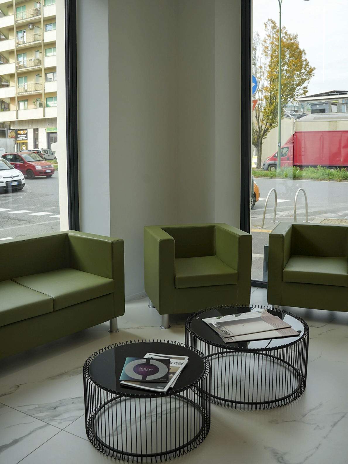 Sala attesa dello showroom Porta Nuova a Torino con sedute verdi, tavolini minimal e interior design contemporaneo luminoso.