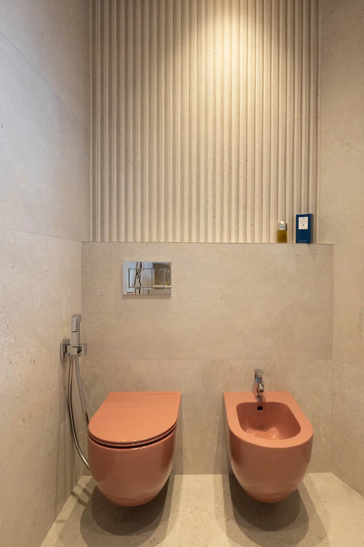 Sanitari rosa sospesi e rivestimenti tridimensionali in un bagno contemporaneo.