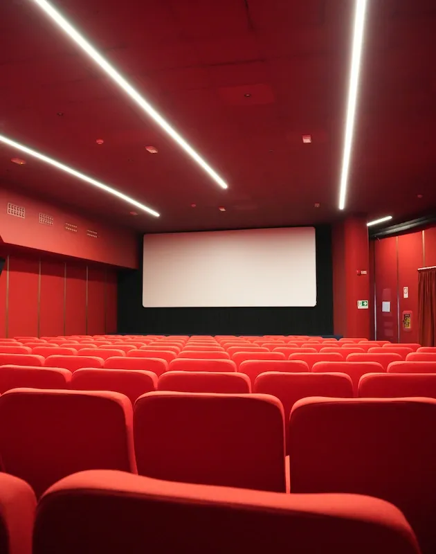 Vista prospettica di una sala cinema moderna con poltrone in velluto rosso, soffitto tecnico coordinato e sistema di illuminazione a LED lineari incassati.
